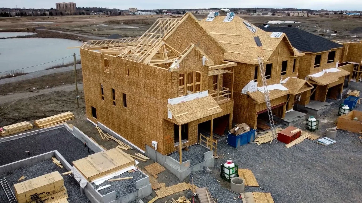 New residential homes under construction with exposed pitched roof trusses, decking and roofing materials